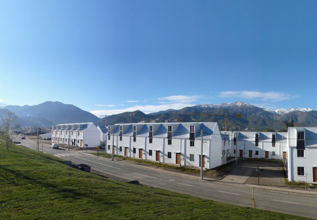 A completed housing development in a rich, green landscape with a large mountain range in the background below a clear, cloud-free sky